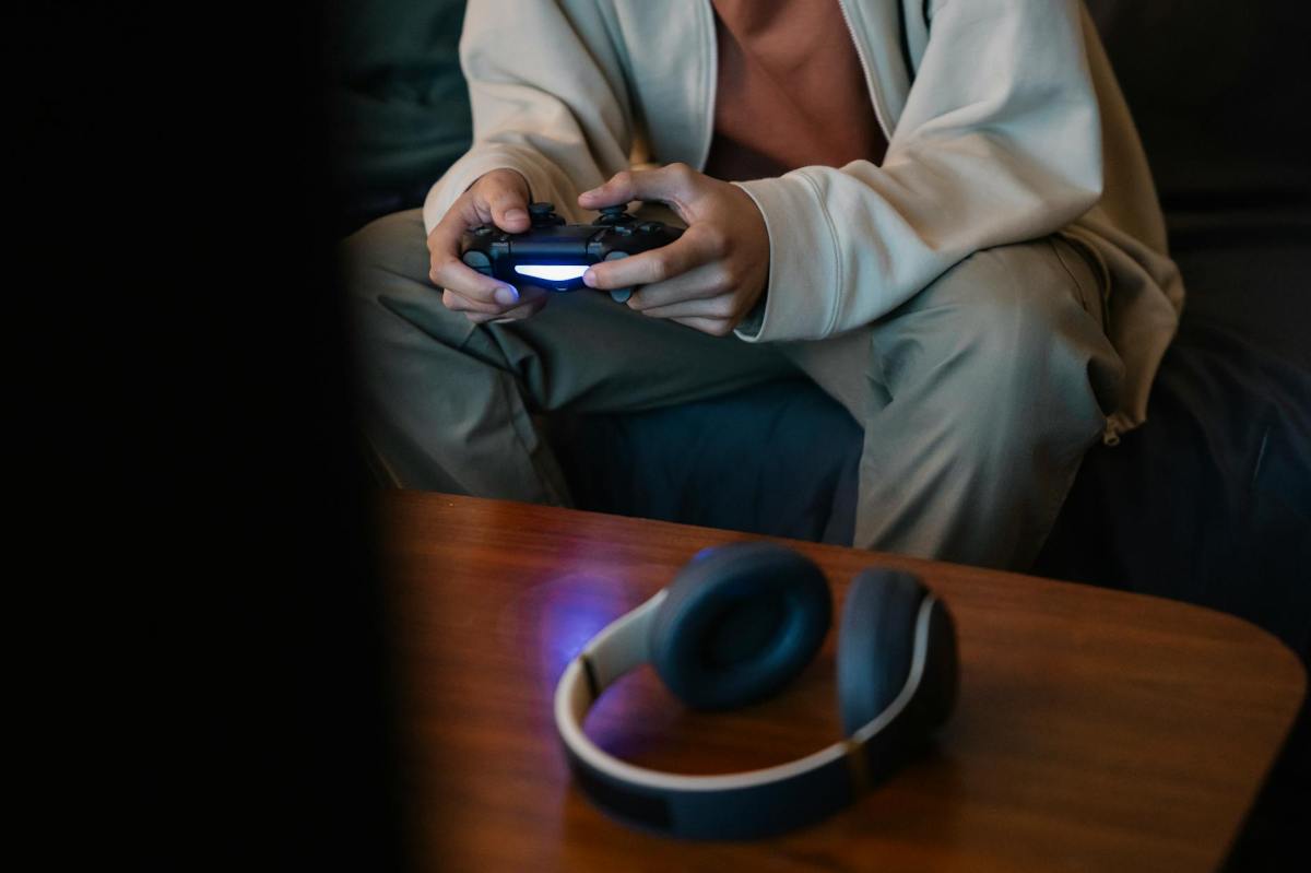 faceless gamer with gamepad against wireless headphones at home