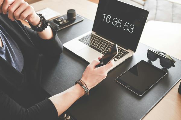 woman using a smartphone while fronting a macbook pro and black ipad